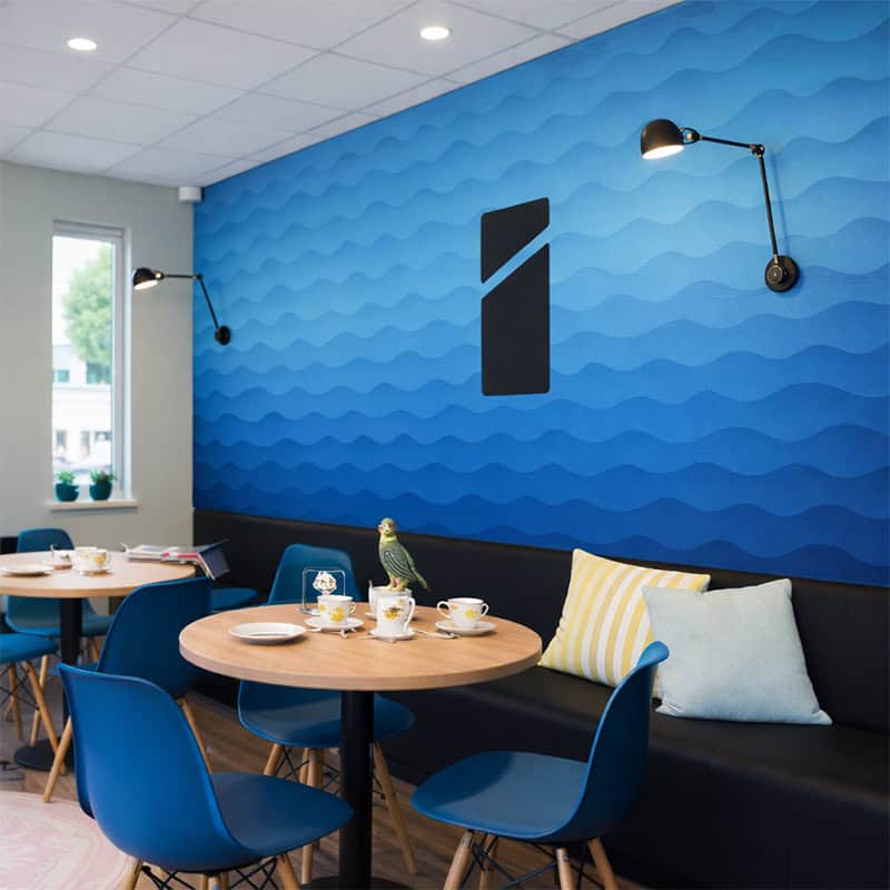 Behang.jpg Blauw behang met golfpatroon en Smid Media Solutions logo op muur in moderne horecaruimte met ronde tafels en blauwe stoelen
