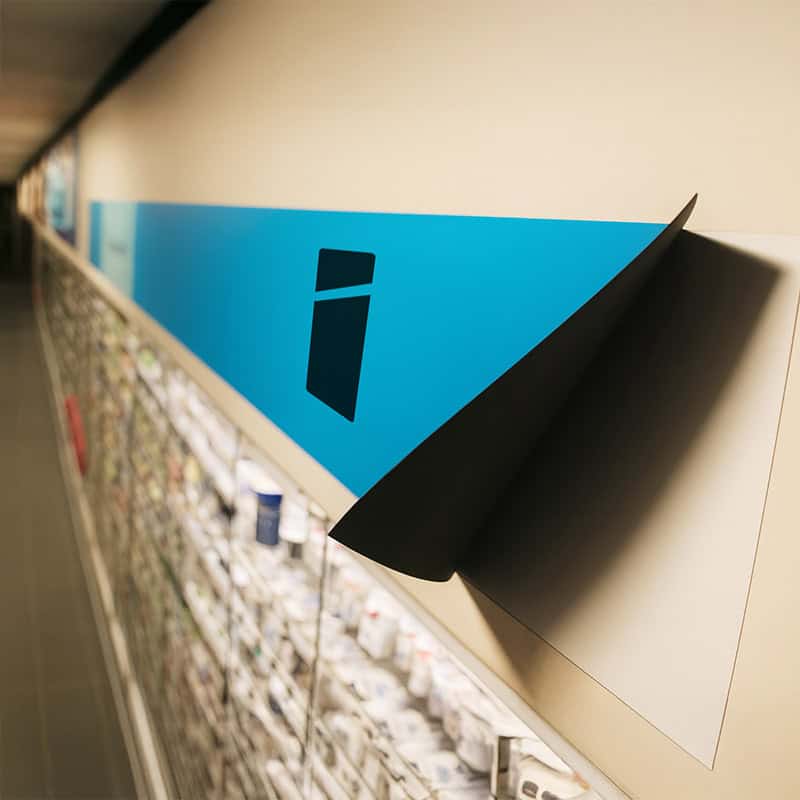 Blauwe magneetfolie met Smid Media Solutions logo deels losgetrokken van wand boven winkelschap