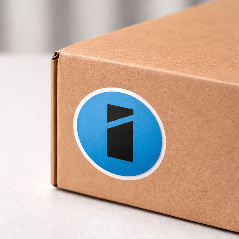 Ronde blauwe vinyl sticker met Smid Media Solutions logo op bruine kartonnen verzenddoos